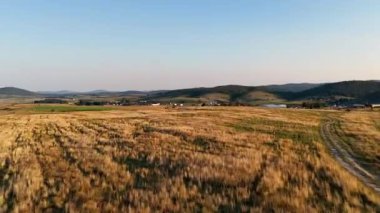 Güneşli tarım alanları ufka doğru uzanıyor. Dağılmış tepeler ve soluk kırsal siluetlerle.