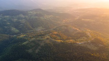 Yumuşak alacakaranlık ormanlık araziye iniyor, sakin bir yaz sisi ile kırsal araziyi kaplıyor.