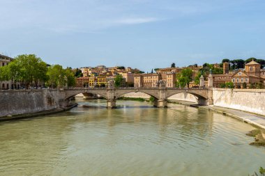Roma, İtalya 'daki Tiber Nehri üzerindeki Ponte Sant Angelo taş köprüsünün arka planında renkli binalar bulunuyor.