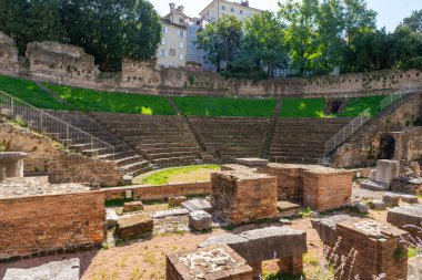 Trieste 'deki antik Roma amfitiyatrosunda taş koltuklar ve harabeler şehir binalarıyla çevrili.