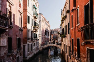 Renkli tarihi binalar arasında küçük bir köprünün altından geçen gondollu Venedik kanalını daralt