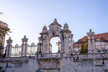 Budin Kalesi 'nin tarihi barok tarzı giriş kapısı. Ayrıntılı detaylar, taş heykeller ve açık mavi gökyüzü altında demir parmaklıklar.