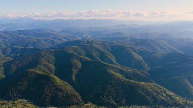 Alp vadilerini ve yazlık gökyüzünün altındaki yeşil orman tepelerini gösteren hava görüntüleri..