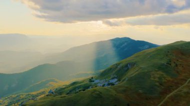 4K hava videosu bulutların arasından geçen ve dağlık vadileri ve tepeleri aydınlatan dramatik güneş ışığını yakalıyor.