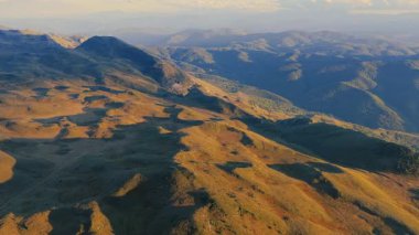 Sıcak altın yaz ışığı altında dağlık tepe ve çayırların 4K görüntülerini süpürüyor.