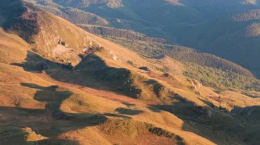Hava 4K görüntüleri, kayalık yamaçlar, çayırlar ve dramatik yaz ışığı ile dağlık tepeleri gösteriyor..