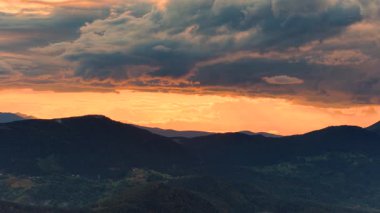 Dağın sırtlarını ve vadilerini çarpıcı renklerle aydınlatan altın günbatımının insansız hava aracı çekimi.