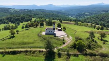 Görüntülerde çayır ve kırsal evlerle çevrili küçük beyaz Ortodoks kilisesi görülüyor..