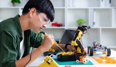 Evde robot kolu ödevi yapan Asyalı genç, robotik programlama teknolojisi ve BTMM eğitim kavramı.