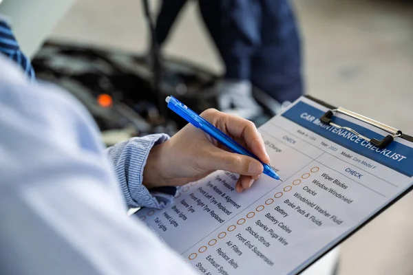 Hand of employee check list to the clipboard insurance while mechanic inspecting car at garage workshop, Car auto services and maintenance check concept.