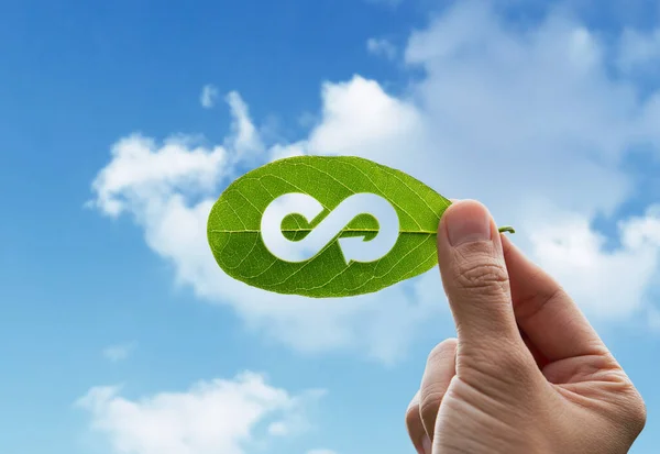 Bir insan eli, çevrenin sürdürülebilir konseptinin iş modeli için sonsuz ve sınırsız enerji içeren dairesel ekonomi ikonu olan yeşil yaprağı tutuyor..