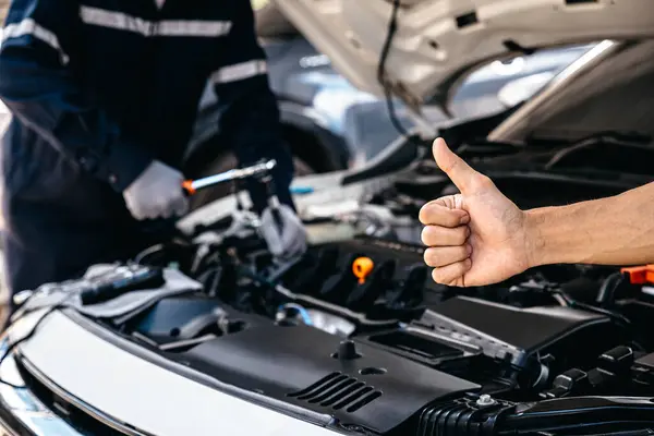 Hand of client showing thumb up for approval of car repair work, Mechanic working under the hood of car.