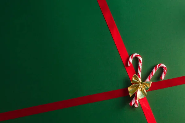 Koyu yeşil arka planda altın kurdeleli Noel şekerleri. Minimum tatil hediyesi konsepti. Düz yat, boşluğu kopyala.