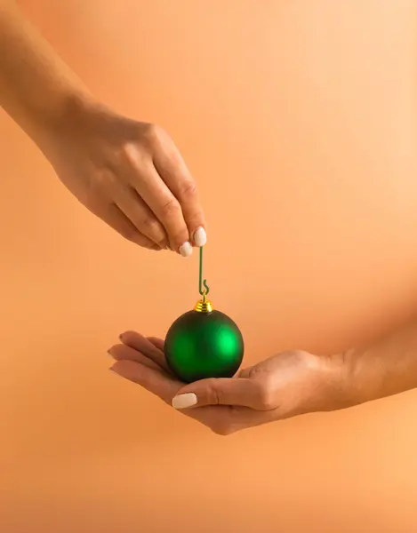 Mãos Mulher Segurando Bugiganga Natal Verde Fundo Laranja Pastel Conceito — Fotografia de Stock