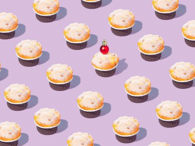 Creative pattern made of cupcake decorated with shiny red Christmas bauble. Trendy concept, collage on a purple pastel background. Creative art minimal aesthetic. Copy space.