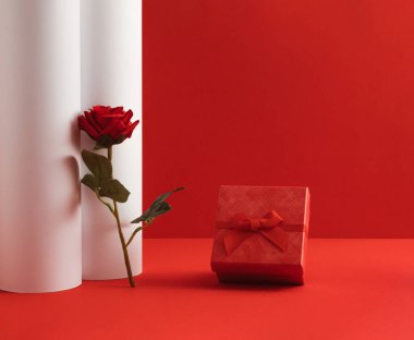Creative Valentine's Day composition with red rose flower and gift box on red and white background. Minimal Women's Day concept.