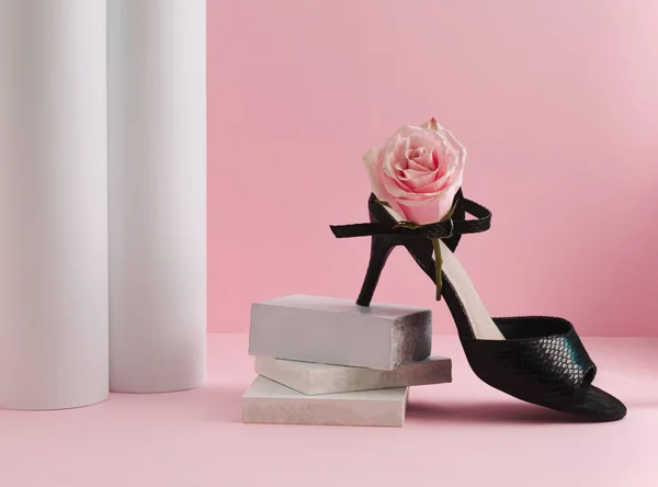Black high heels and pink rose flower on pastel pink background. Environmental protection and sustainability idea. Minimal sustainable fashion concept.