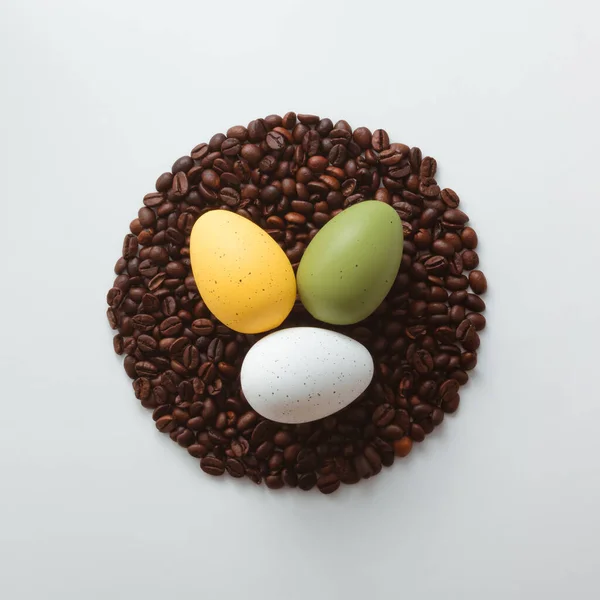 Colorful Easter eggs and coffee roasted beans on white background. Flat lay, top view. Minimal Easter holiday composition.