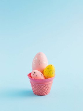 Pastel mavi arka planda renkli yumurtalı dondurma külahı. Asgari Paskalya konsepti. Mutlu Paskalyalar.