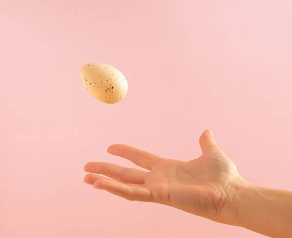 Woman\'s hand throwing away white egg on pastel pink background. Minimal Easter concept.