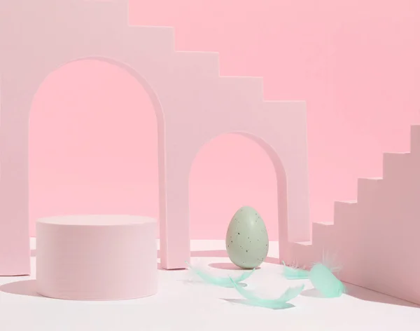 Podium, stand for product presentation, pastel green Easter egg and feathers on pink background. Mockup for branding and festive packaging presentation. Modern aesthetic.