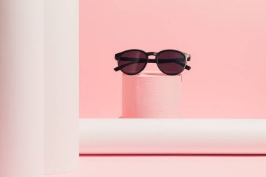 Ürün podyumunda siyah güneş gözlüğü. Pastel pembe arka planda Ürün Gösterimi ve İş Konsepti için uygundur. Moda konsepti.