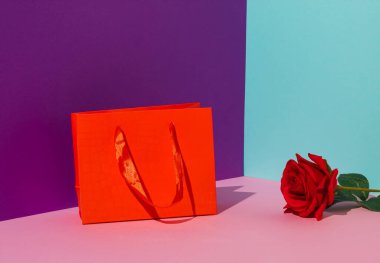 Creative anniversary celebration arrangement with vivid background. Minimal Valentines Day concept made with red bag and red rose flower.