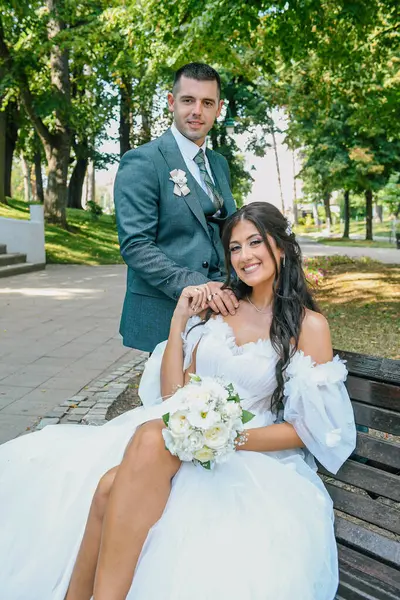 Çekici bir düğün çifti bankta oturur. Güzel gelin ve damat açık havada huzurlu bir anın tadını çıkarıyorlar..