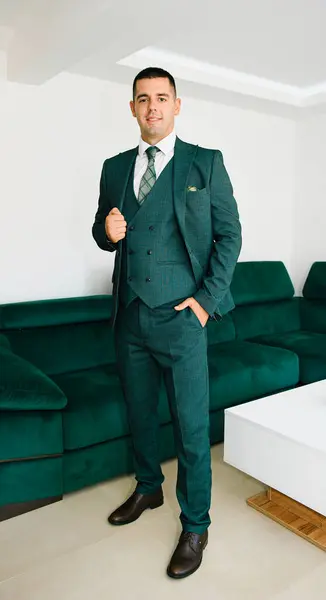 Modern bir portre ortamında yeşil takım giyen zarif ve kendine güvenen bir damat. Düğün organizasyonu için şık ve mutlu bir adam, stüdyoda evlilik töreni..