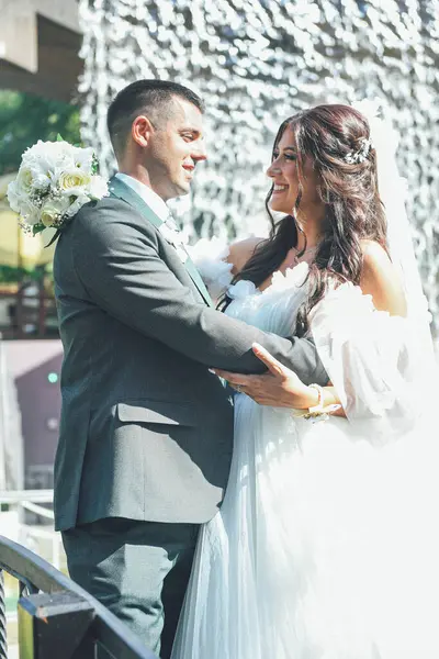 Gelin ve damat açık havada huzurlu bir anın tadını çıkarıyorlar. Genç çift düğün günlerinde romantik bir sahnede sarılırlar. Arka planda doğa ve şelale vardır..