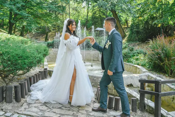 Güzel bir gelin ve damat açık havada huzurlu bir anın tadını çıkarıyor. Damat düğün günlerinde gelinin elini romantik bir sahnede tutar. Havada aşk kokusu var..