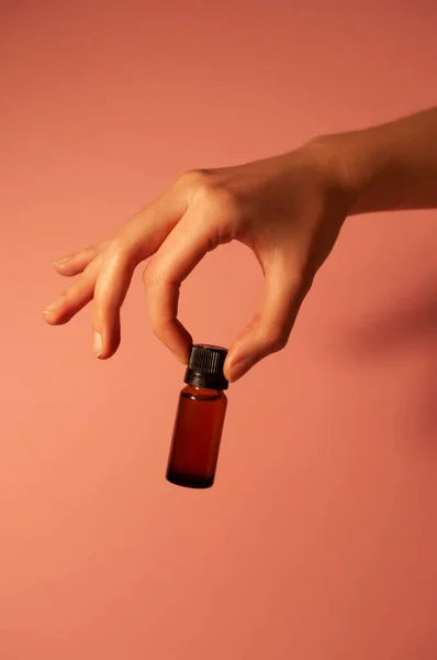 Kız, şeftali arkaplanına karşı yüz serumunu elinde tutuyor. Güzel bir kavanoz serum..