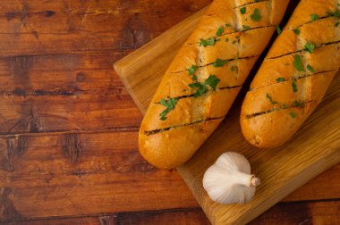Tahta bir masanın üzerinde ahşap bir tahtanın üzerinde aromatik bitkilerle taze peynirli sarımsaklı ekmek yakın plan. Üst görünüm.
