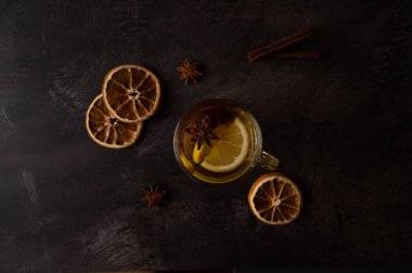 Limon dilimli siyah çay, siyah metalik arka planda cam bir fincanda yıldız anason ve tarçın. Üst görünüm.