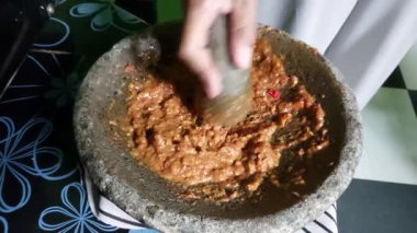 Bir kadın kırmızı biber ve baharat öğütüyor, karışımı iyi ezilmiş gibi görünüyor. Endonezya 'dan örnekler.
