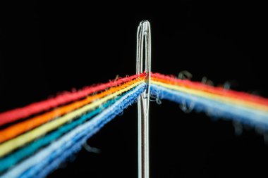 multi-colored threads for sewing in the form of a rainbow pass through an antique needle on a black background close-up