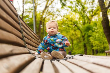 Parkta bir bankta sabun köpüğü yakalayan küçük bir çocuğun portresi.