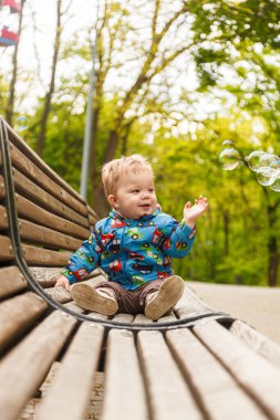 portrait of a little boy in the park on a bench catching soap bubbles close-up