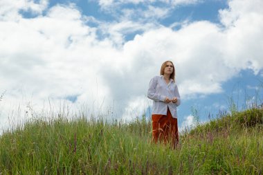 Beyaz gömlekli ve turuncu etekli güzel kız mavi gökyüzüne ve bulutlara karşı