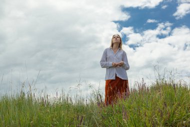 Beyaz gömlekli ve turuncu etekli güzel kız mavi gökyüzüne ve bulutlara karşı