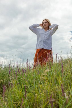 Beyaz gömlekli ve turuncu etekli güzel kız mavi gökyüzüne ve bulutlara karşı