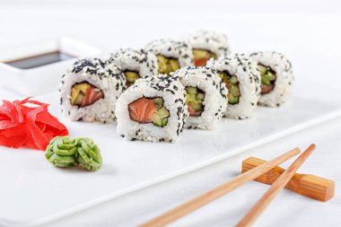 Sushi with salmon on a white plate with wasabi, ginger, soy, chopsticks on a white background close-up