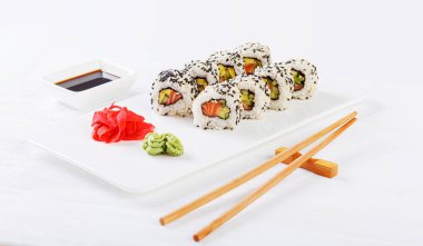 Sushi with salmon on a white plate with wasabi, ginger, soy, chopsticks on a white background close-up