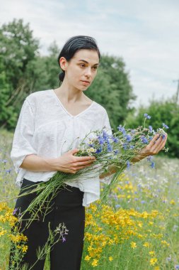 Yaz tarlalarının arasında kır çiçekleriyle güzel bir kız.