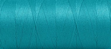 Texture of threads in a spool of turquoise color on a white background close-up