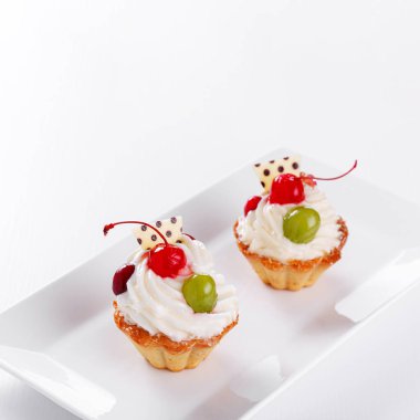 Beyaz arka planda vişneli ve üzümlü güzel kremalı pastalar.