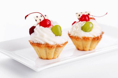 Beyaz arka planda vişneli ve üzümlü güzel kremalı pastalar.