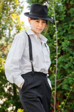 Şapkalı, beyaz gömlekli, siyah pantolonlu, askılı güzel bir kız.