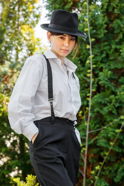 Şapkalı, beyaz gömlekli, siyah pantolonlu, askılı güzel bir kız.