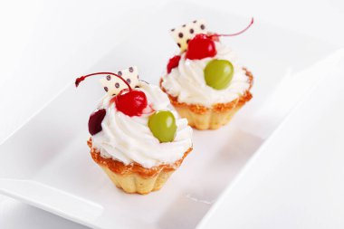 Beyaz arka planda vişneli ve üzümlü güzel kremalı pastalar.